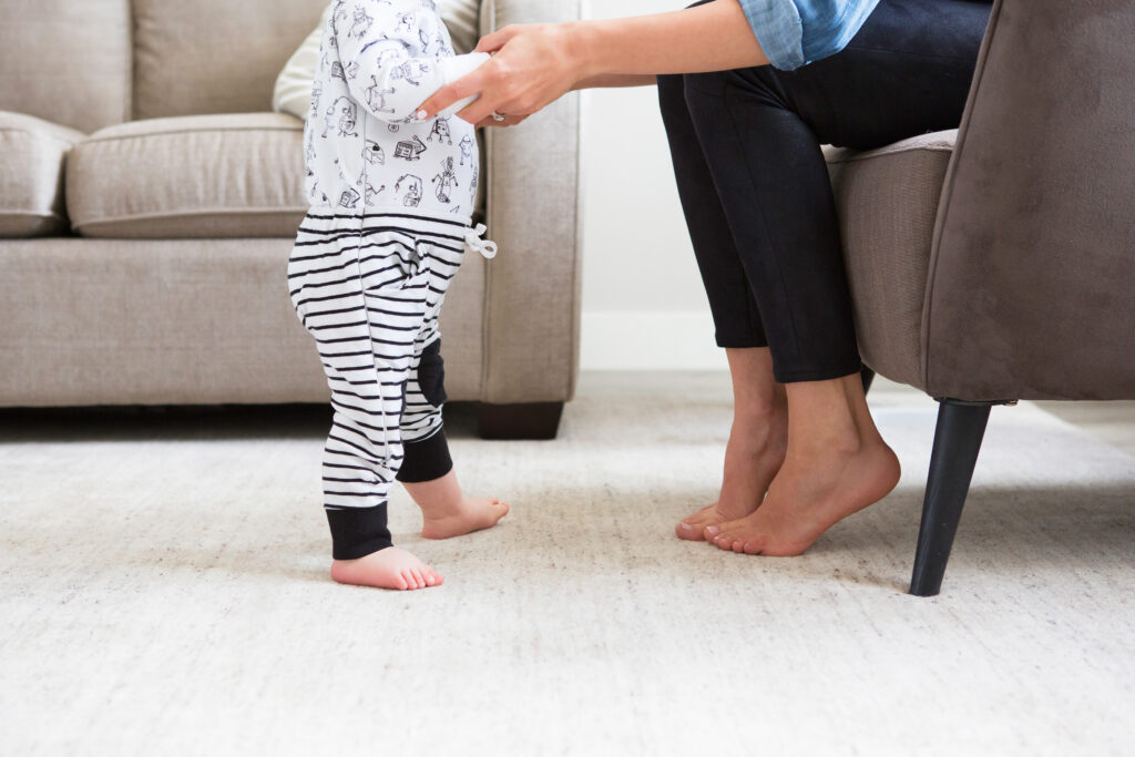 Mother helping baby take first steps on a clean, cozy living room rug