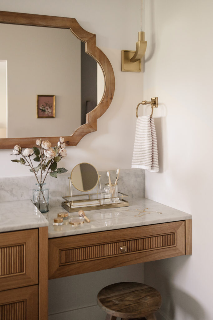 Warm wood bathroom vanity with a marble countertop, brass accents, and soft natural light on a calm neutral wall.