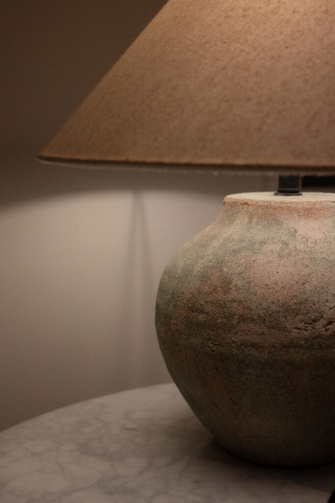 Textured table lamp with a warm-toned shade casting soft ambient light on a bedside table.